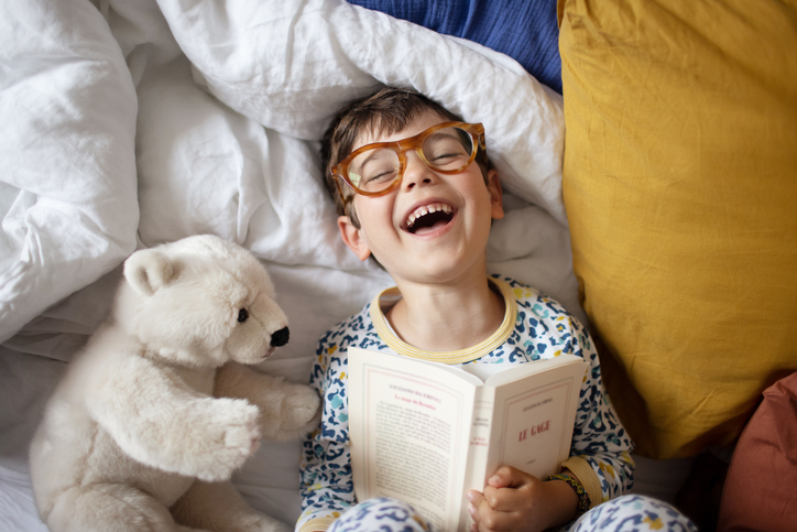 A 4 year old little boy having fun, laying on a bed